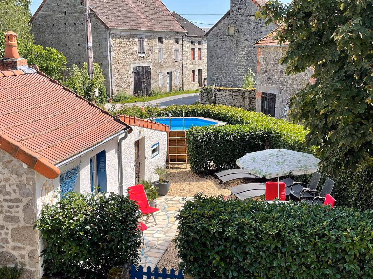 Uitzicht over de tuin met zwembad, ligstoelen en parasol, met daarachter de stenen huizen van het dorp