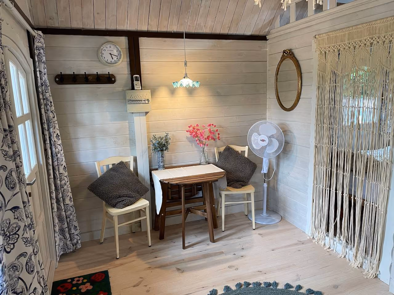 Interieur met witte houten wanden, een klaptafel voor twee, ventilator en macramégordijnen voor de deur