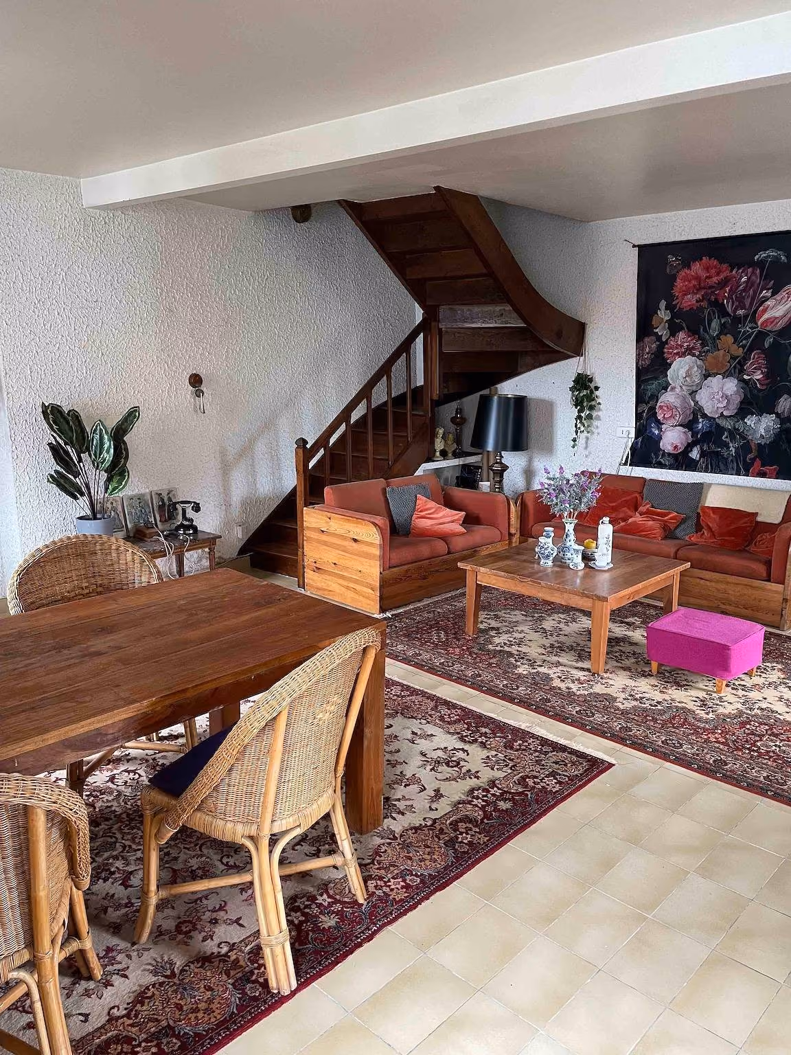 Woonkamer met houten trap, roodbruine banken, eettafel en Perzische tapijten op een tegelvloer