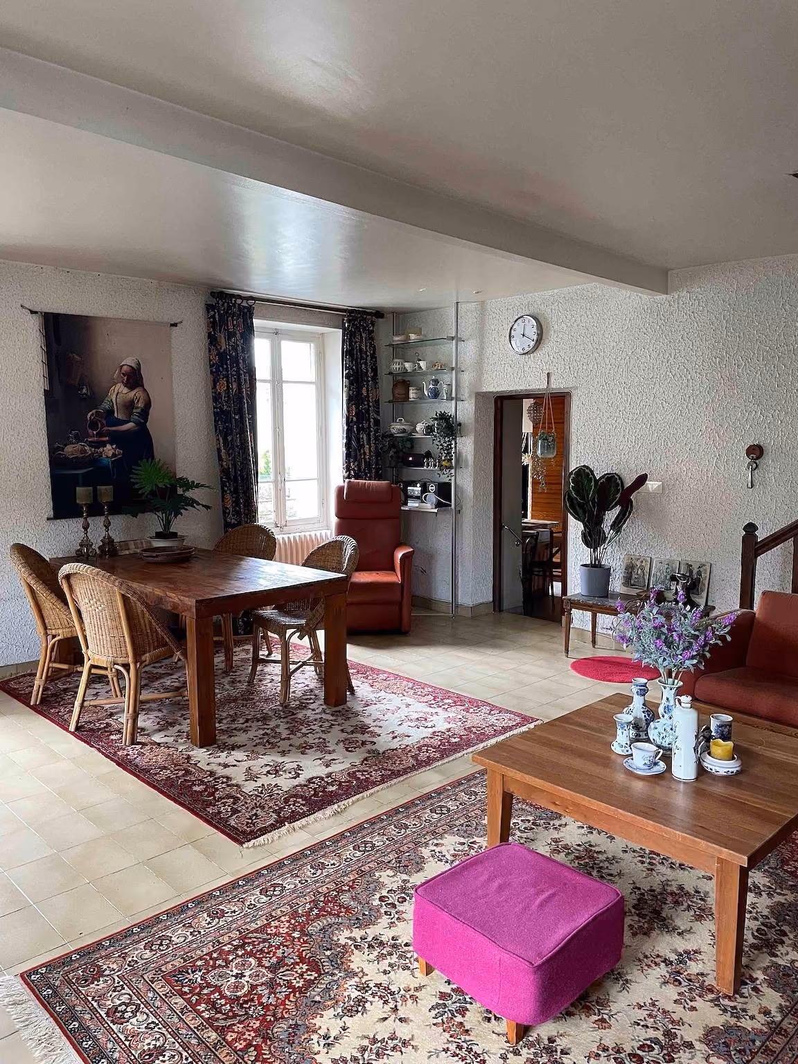 Woon- en eetkamer met houten eettafel, rieten stoelen, tapijten en een raam aan de straatzijde