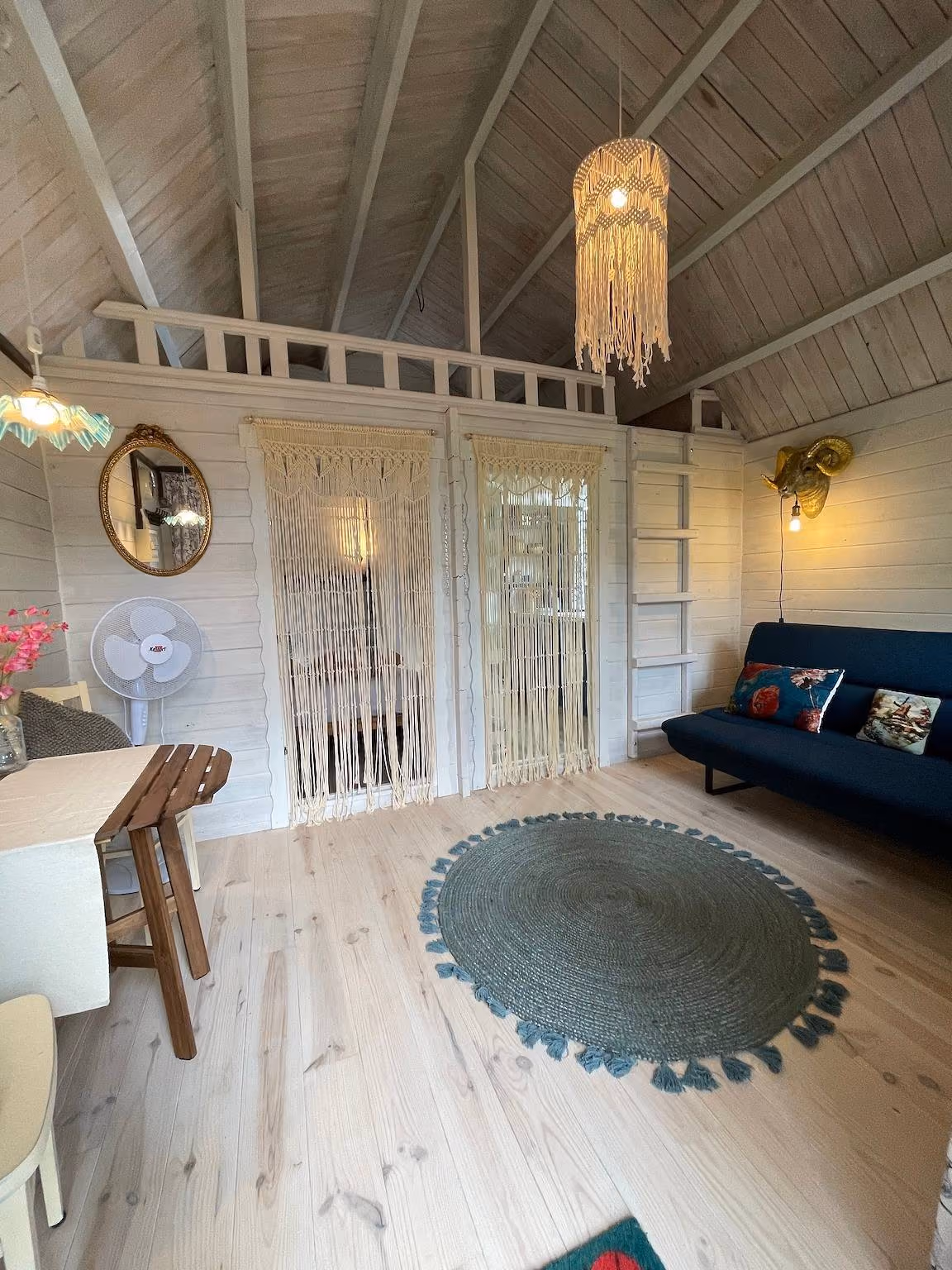 Zithoek met blauwe slaapbank, rond vloerkleed en een mezzanine onder de hoge witte houten kap