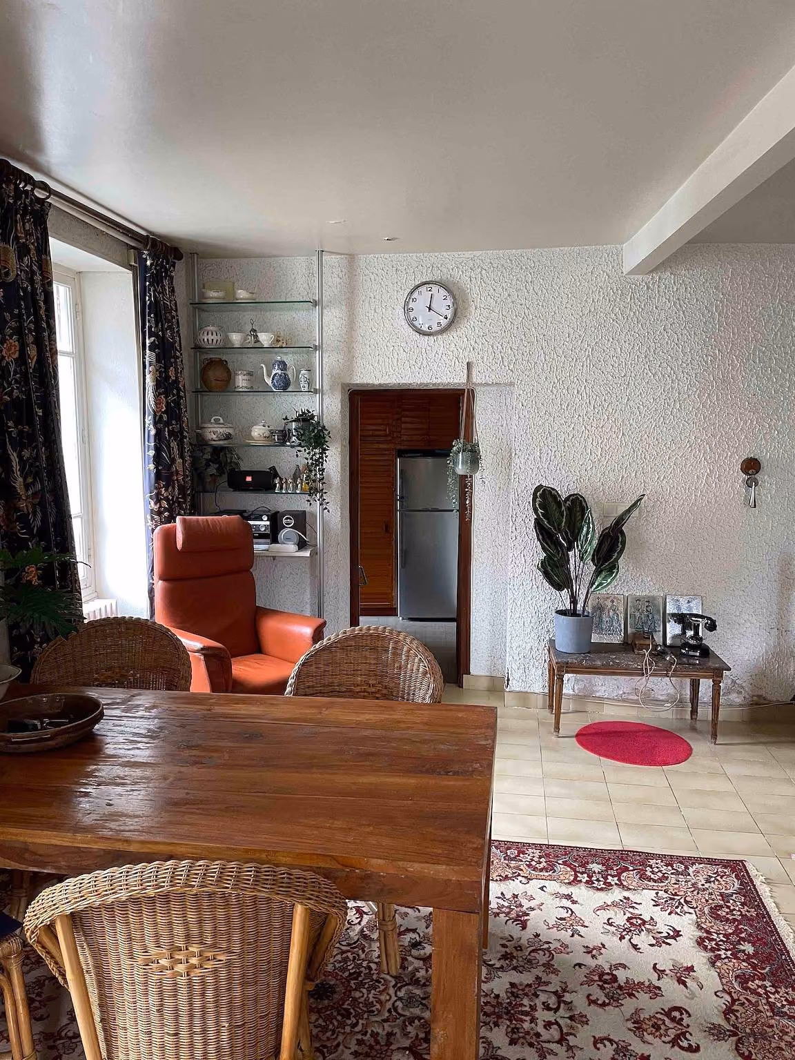 Eethoek met houten tafel, rieten stoelen en een open keuken met koelkast op de achtergrond