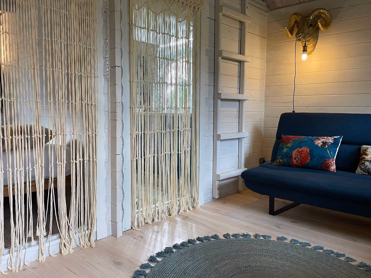 Zitgedeelte met blauwe bank, macramégordijn en een houten ladder naar de mezzanine