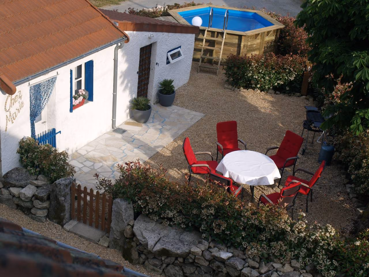 Luchtfoto van het rond zwembad en het terras met tafel en stoelen, omgeven door een border met struiken