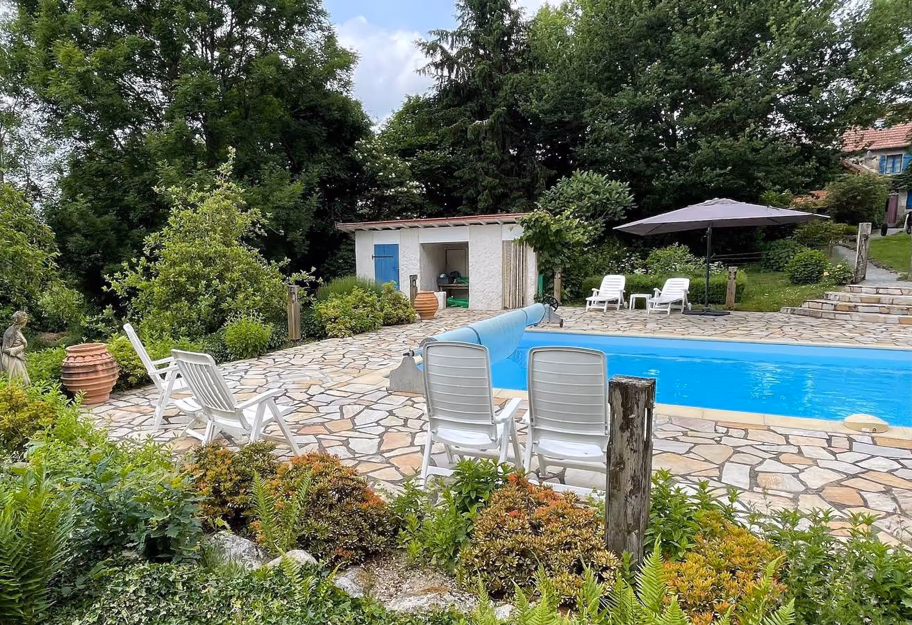Zwembad gezien vanaf het terras, met ligstoelen, een parasol en het poolhouse op de achtergrond